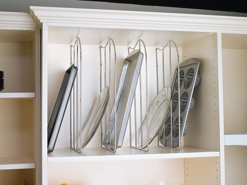 Chrome wire tray divider installed in kitchen cabinet, organizing baking sheets, muffin pans, and glass trays vertically